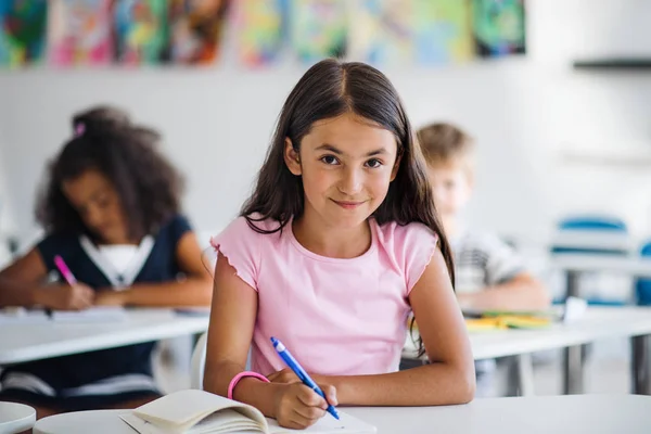 Маленькая школьница, сидящая за столом в классе, смотрит в камеру . — стоковое фото