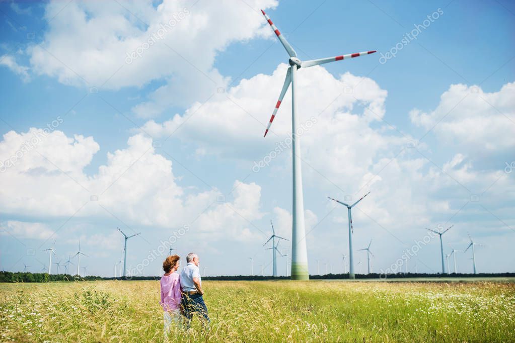 Senior couple walking on field on wind farm. Copy space.