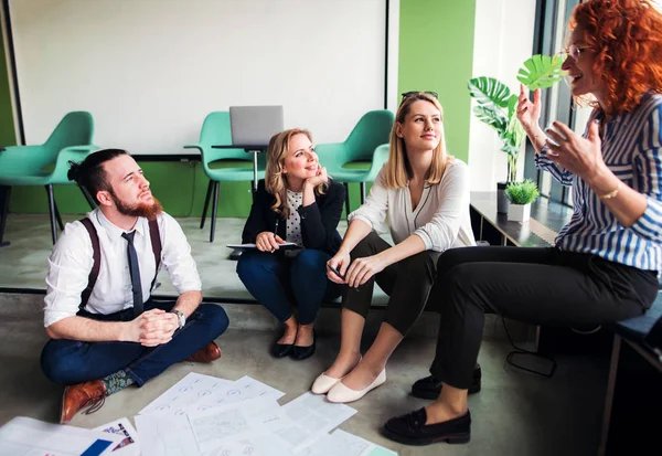 Een groep jonge zakenmensen die in een kantoor op de vloer zitten, praten. — Stockfoto