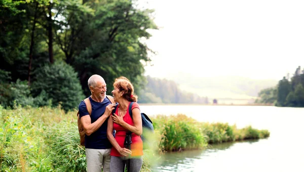 Senior turist par på en promenad i naturen, stående vid sjön. — Stockfoto