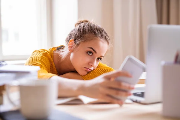 Uma jovem estudante sentada à mesa, usando smartpone ao estudar . — Fotografia de Stock