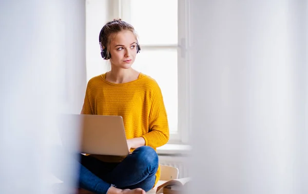 Młoda studentka siedząca na biurku, przy użyciu słuchawek podczas studiowania. — Zdjęcie stockowe