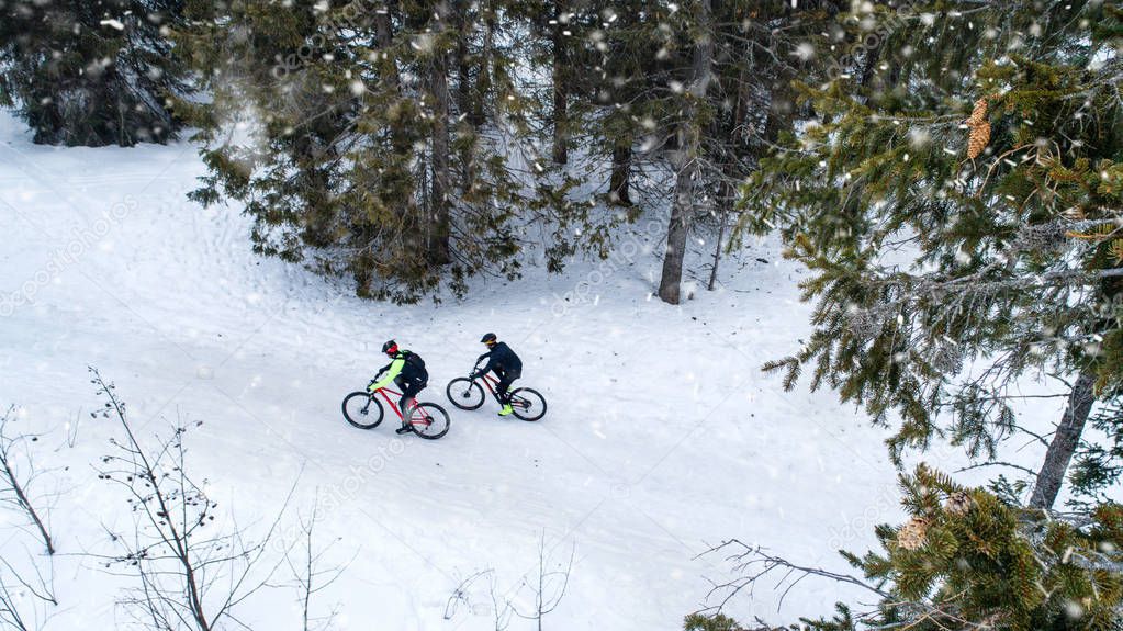 Aerial view of two mountain bikers riding on road in forest outdoors in winter.