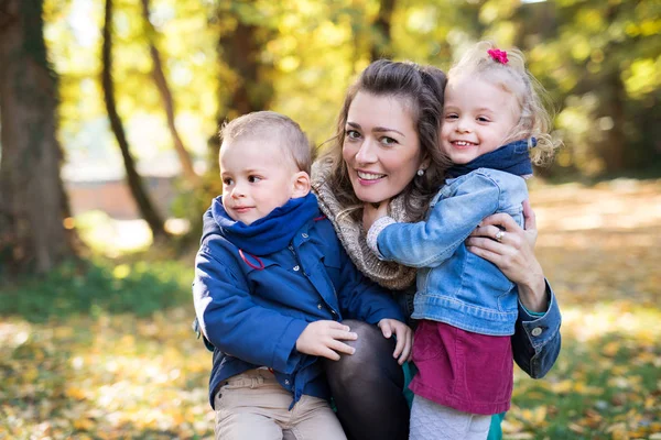 Mooie jonge moeder met kleine tweeling op een wandeling in herfst bos. — Stockfoto