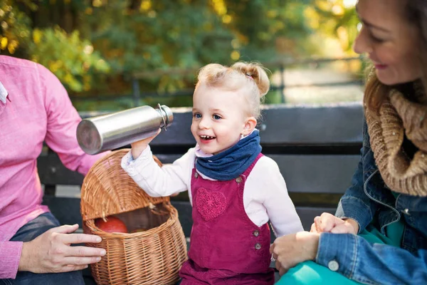 Vacker ung familj med liten daugther sittande på bänken i höst parken. — Stockfoto