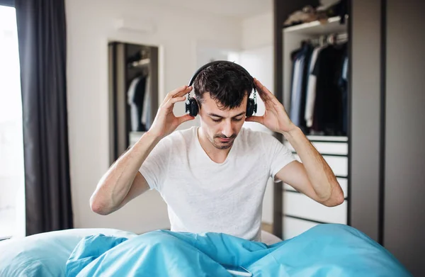 Jovem com fones de ouvido na cama em casa, ouvindo música . — Fotografia de Stock