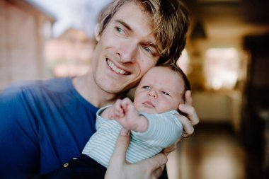 Evde yeni doğmuş bir bebek tutan genç bir baba.