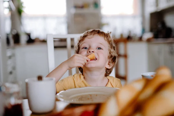 Une vue de face d'un tout-petit garçon qui mange à la maison . — Photo