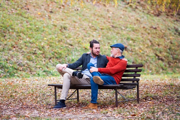 Старший отец и его сын сидят на скамейке на природе и разговаривают . — стоковое фото