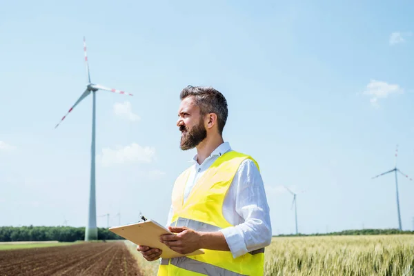 An engineer standing on a field on wind farm, making notes. — Stock Photo, Image