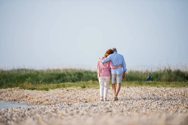 Blick von hinten auf ein älteres Ehepaar im Urlaub bei einem Spaziergang am See,. — Stockfoto