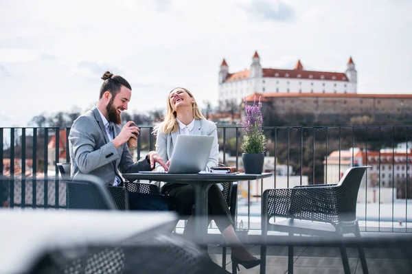 Två unga affärsfolk med laptop sitter på en terrass utanför kontoret, skrattar. — Stockfoto