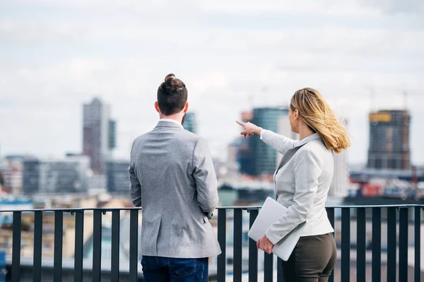 Dois jovens empresários com laptop em pé em um terraço fora do escritório, conversando . — Fotografia de Stock