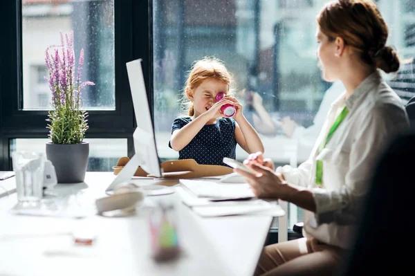 Eine Geschäftsfrau mit kleiner Tochter sitzt in einem Büro und arbeitet. — Stockfoto