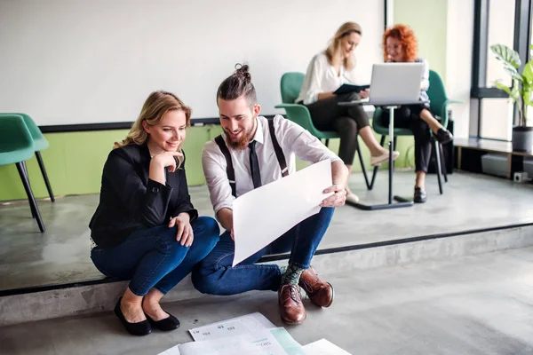 Eine Gruppe junger Geschäftsleute sitzt auf dem Fußboden in einem Büro und spricht. — Stockfoto