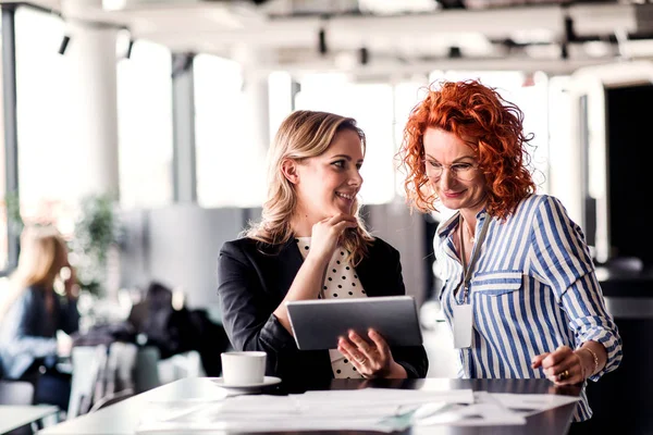 Zwei Geschäftsfrauen mit Tablet sitzen in einem Büro und unterhalten sich. — Stockfoto