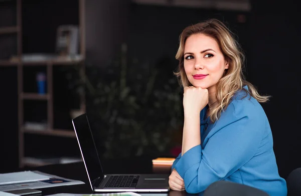 Junge Geschäftsfrau mit Laptop sitzt in einem Büro und blickt in die Kamera. — Stockfoto
