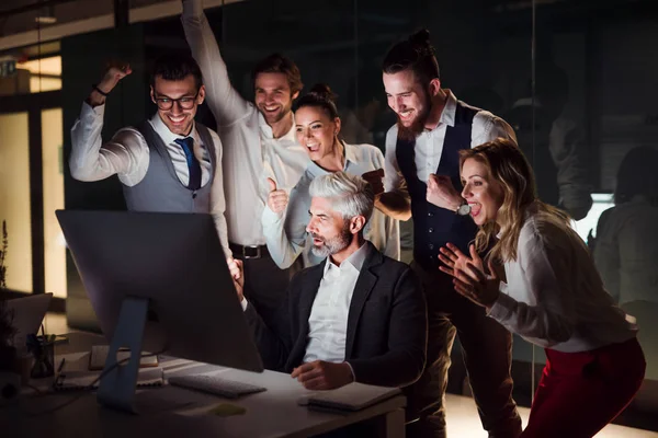 Un grupo de empresarios en una oficina por la noche, expresando emoción . — Foto de Stock