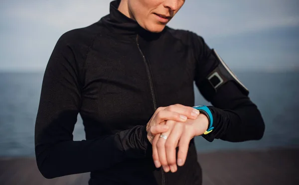 Uma jovem esportista de pé ao ar livre na praia, usando smartwatch . — Fotografia de Stock