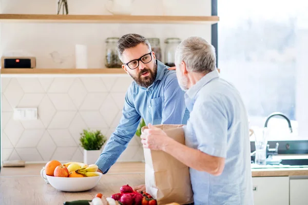 En vuxen hipster son och Senior far inomhus hemma, uppackning shopping. — Stockfoto