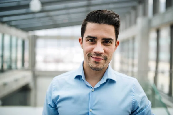 Um retrato de um jovem empresário em pé dentro de um escritório . — Fotografia de Stock