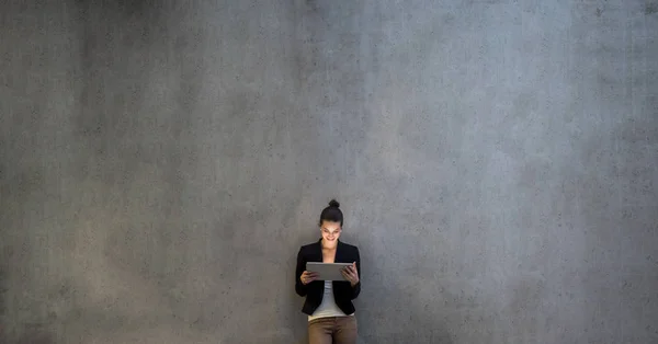 Wanita bisnis muda dengan tablet berdiri menghadap dinding beton di kantor . — Stok Foto