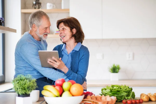 Un retrato de pareja de ancianos enamorados en el interior de su casa, utilizando una tableta . —  Fotos de Stock