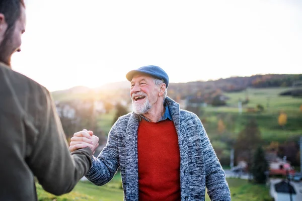 Smích staršího otce a jeho syna při chůzi v přírodě, potřásaje si rukama. — Stock fotografie