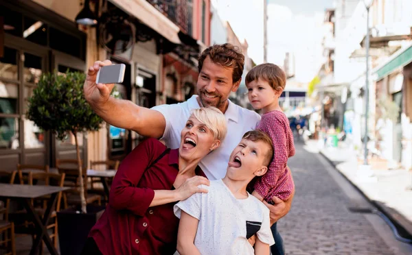 Eine junge Familie mit zwei kleinen Kindern steht draußen in der Stadt und macht ein Selfie. — Stockfoto