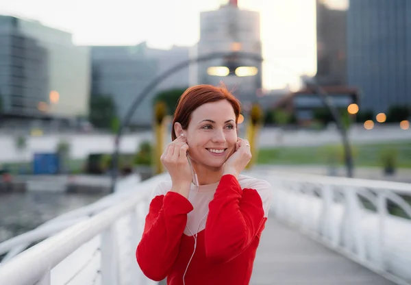 Front view of young woman runner with earphones in city, resting. — Stock Photo, Image