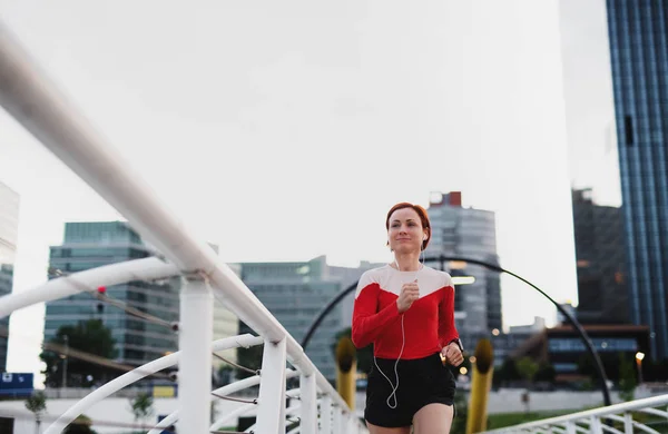 市内でジョギングイヤホンを持つ若い女性ランナーの正面図. — ストック写真