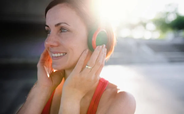 A close-up of young woman runner with headphones in city, resting. — Stock Photo, Image