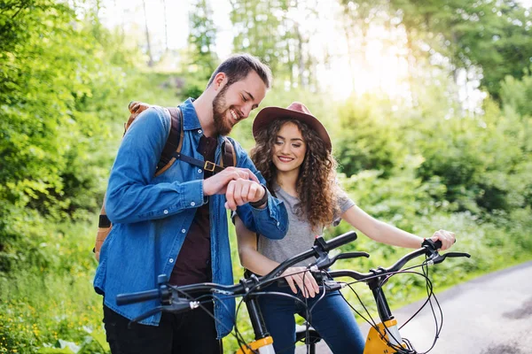 Jovens turistas casal viajantes com scooters elétricos na natureza, usando smartwatch . — Fotografia de Stock