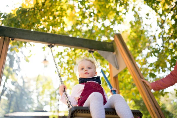 Una niña pequeña con un padre irreconocible en un columpio en un parque infantil . —  Fotos de Stock