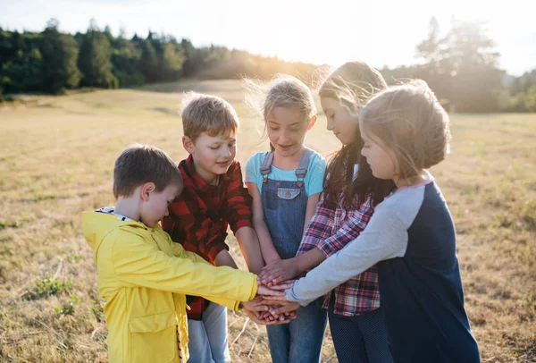 Sekelompok anak-anak sekolah berdiri di lapangan perjalanan di alam, meletakkan tangan bersama-sama . — Stok Foto
