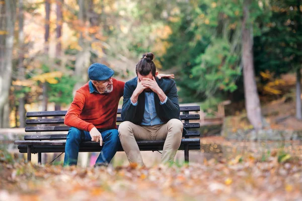 Senior far tröstande hans sorgliga vuxna son på bänken i naturen. — Stockfoto