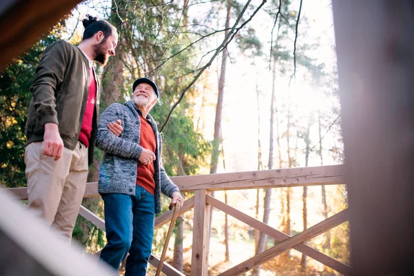 Padre anziano con bastone da passeggio e suo figlio a passeggio nella natura, parlando . — Foto Stock