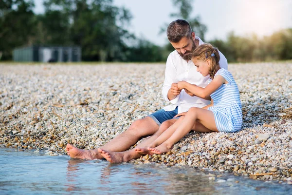 Vista lateral do pai e da filha pequena em um feriado sentado junto ao lago . — Fotografia de Stock