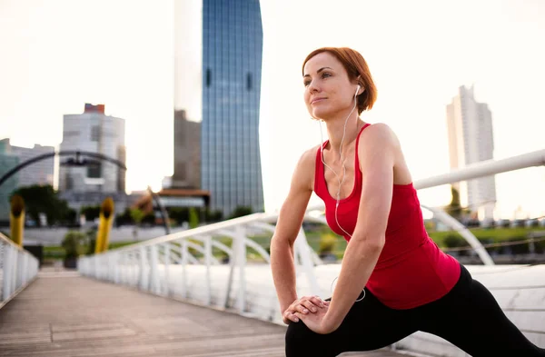 Giovane donna corridore con auricolari in città, stretching . — Foto Stock