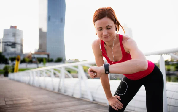 Młoda kobieta biegacz z słuchawek w mieście, za pomocą zegarka SmartWatch. — Zdjęcie stockowe