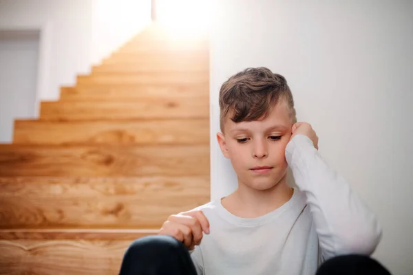 Um rapazinho infeliz sentado no chão junto às escadas. Espaço de cópia . — Fotografia de Stock