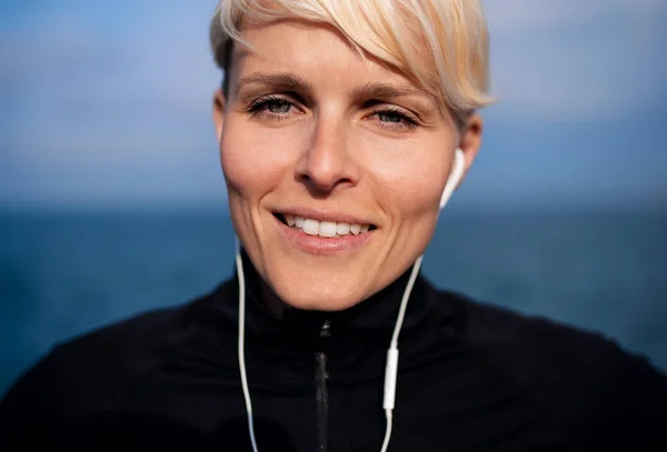 一张年轻女运动员的画像，她带着耳机站在户外的海滩上. — 图库照片