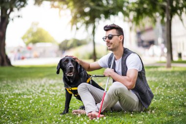 Beyaz baston ve rehber köpek şehirde parkta oturan genç kör adam.