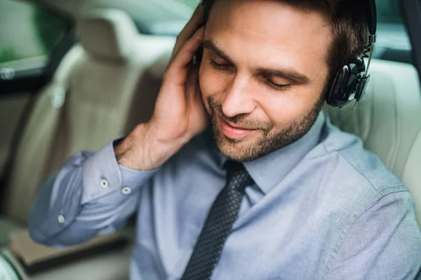 Young happy business man with headphones, shirt and tie sitting in car. — Stock Photo, Image