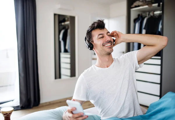 Young man with headphones and smartphone in bed at home, listening to music. — Stock Photo, Image