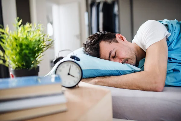 自宅のベッドで目覚まし時計を持つ若い男, 睡眠. — ストック写真