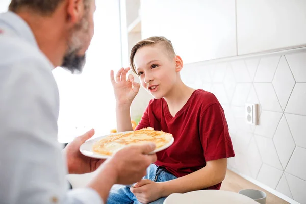 Mature father with small son indoors in kitchen, making pancakes. — Stock Photo, Image