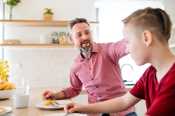 Mogen far med liten son inomhus sitter vid bordet, äta pannkakor. — Stockfoto