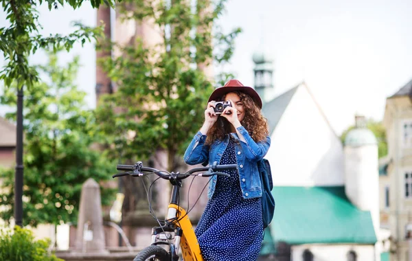 Küçük bir kasabada elektrikli scooter ile güzel genç kadın turist, kamera kullanarak. — Stok fotoğraf