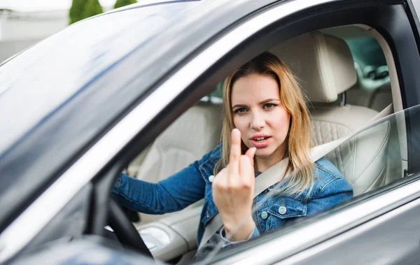 Boze jonge vrouw bestuurder zittend in auto, tonen van middelvinger. — Stockfoto